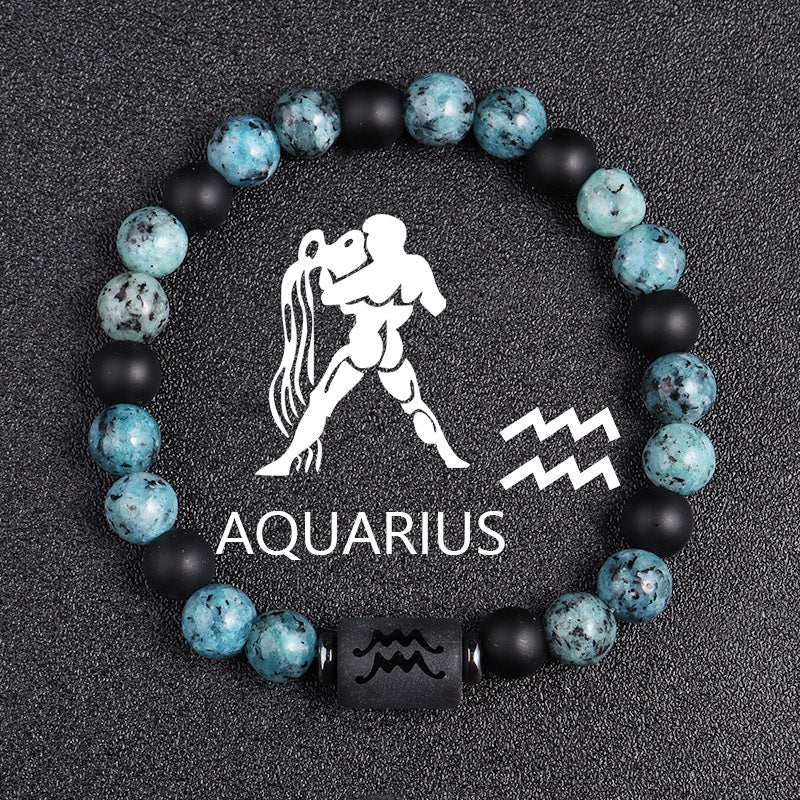 Zodiac bracelet, Aquarius option, with blue-green jasper, matte black onyx, hematite spacers, and a black Aquarius centerpiece, shown in a focused full product view on dark fabric.