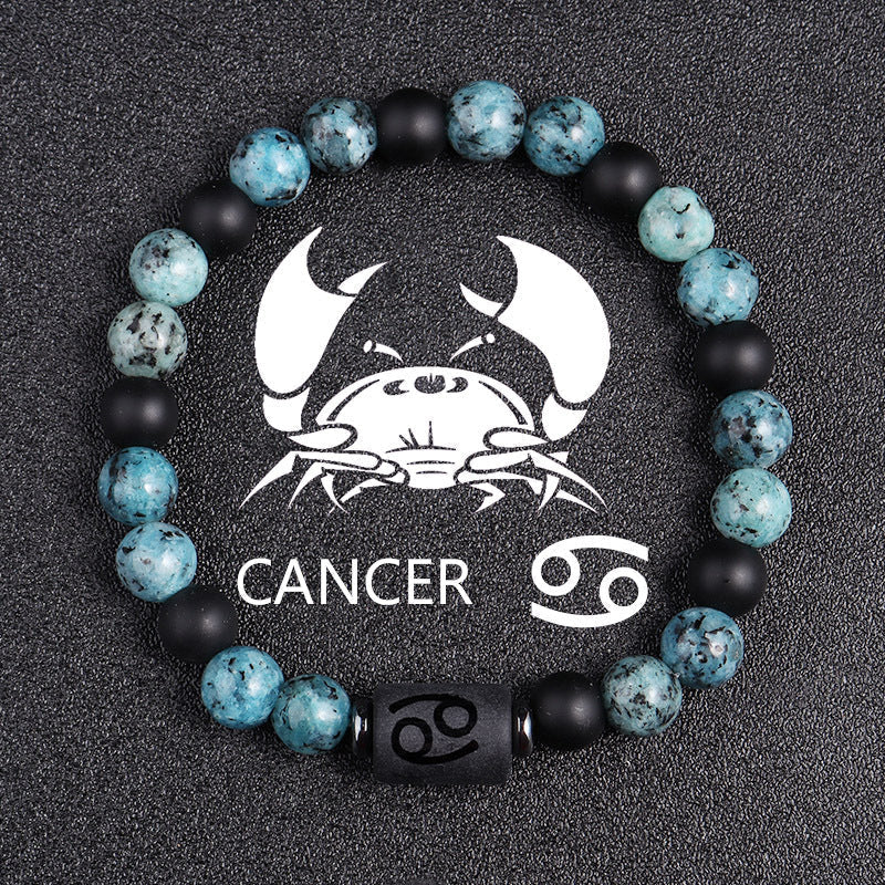 Zodiac bracelet, Cancer option, with blue-green jasper, matte black onyx, hematite spacers, and a black Cancer centerpiece, shown in a detailed focused product view on dark fabric.