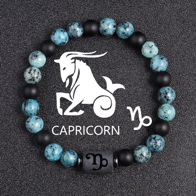 Zodiac bracelet, Capricorn option, with blue-green jasper, matte black onyx, hematite spacers, and a black Capricorn centerpiece, shown in a clear full product view on dark fabric.