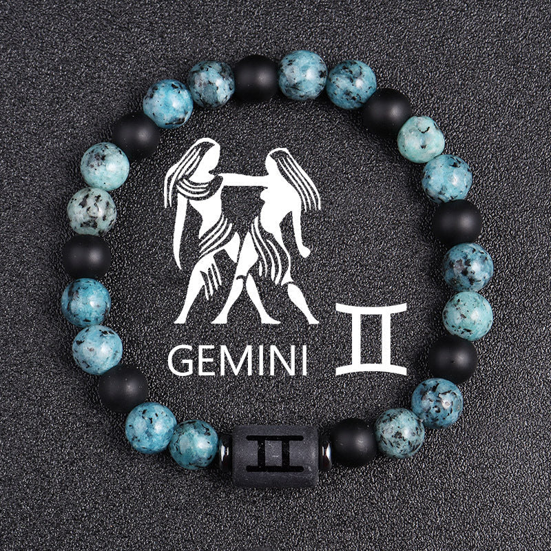 Zodiac bracelet, Gemini option, with blue-green jasper, matte black onyx, hematite spacers, and a black Gemini centerpiece, shown in a detailed focused product view on dark fabric.