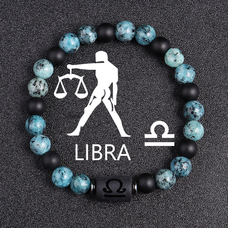 Zodiac bracelet, Libra option, with blue-green jasper, matte black onyx, hematite spacers, and a black Libra centerpiece, shown in a clear focused full product view on dark fabric.