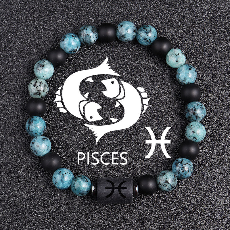 Zodiac bracelet, Pisces option, with blue-green jasper, matte black onyx, hematite spacers, and a black Pisces centerpiece, shown in a detailed focused product view on dark fabric.
