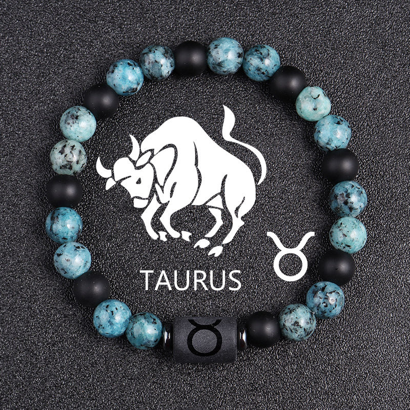 Zodiac bracelet, Taurus option, with blue-green jasper, matte black onyx, hematite spacers, and a black Taurus centerpiece, shown in a detailed focused product view on dark fabric.
